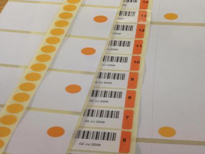 Sheets of white labels with orange gamma indicator dots and sequential barcodes laid out in rows.