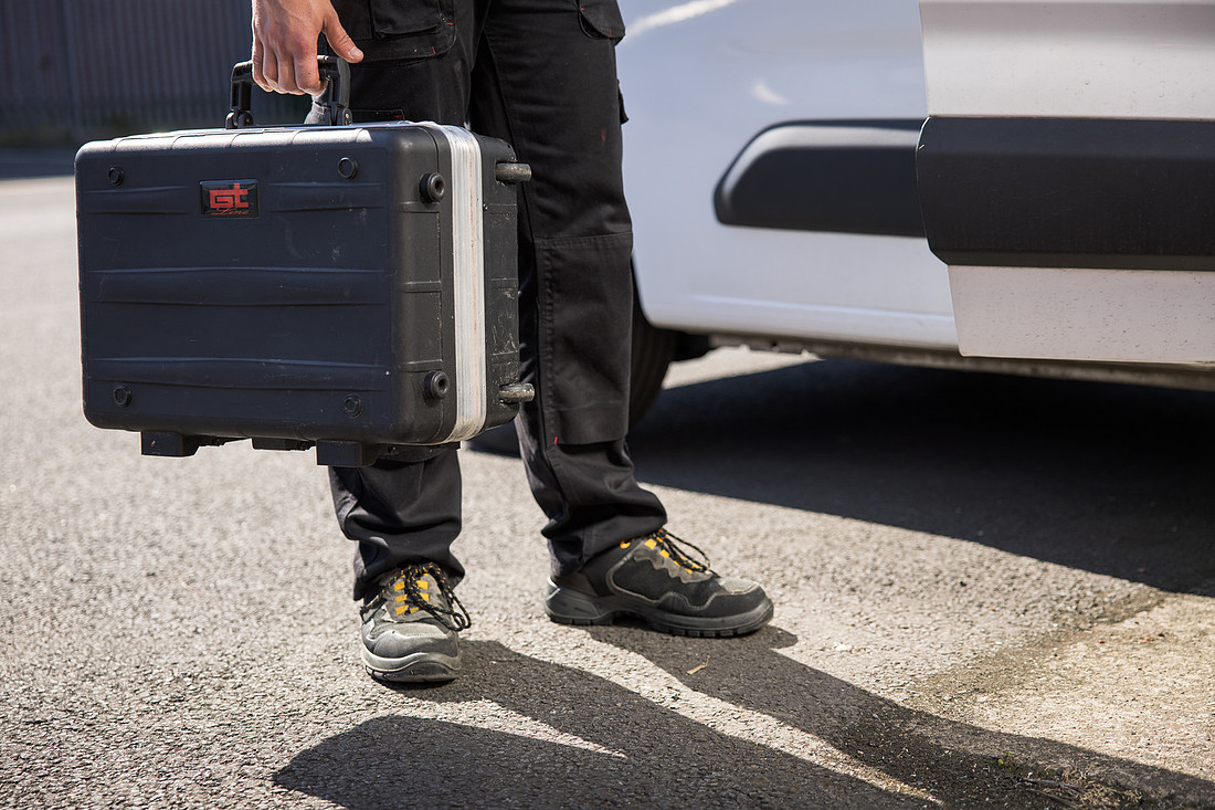 A tool case carried past the branded Sessions UK van, cropped mid-thigh down: legs, work boots and a hand on the case handle.